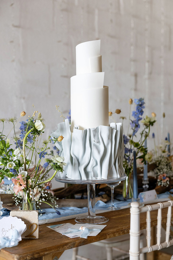 Three-tier white wedding cake with baby blue ruffles on bottom tier by YiShi Cake